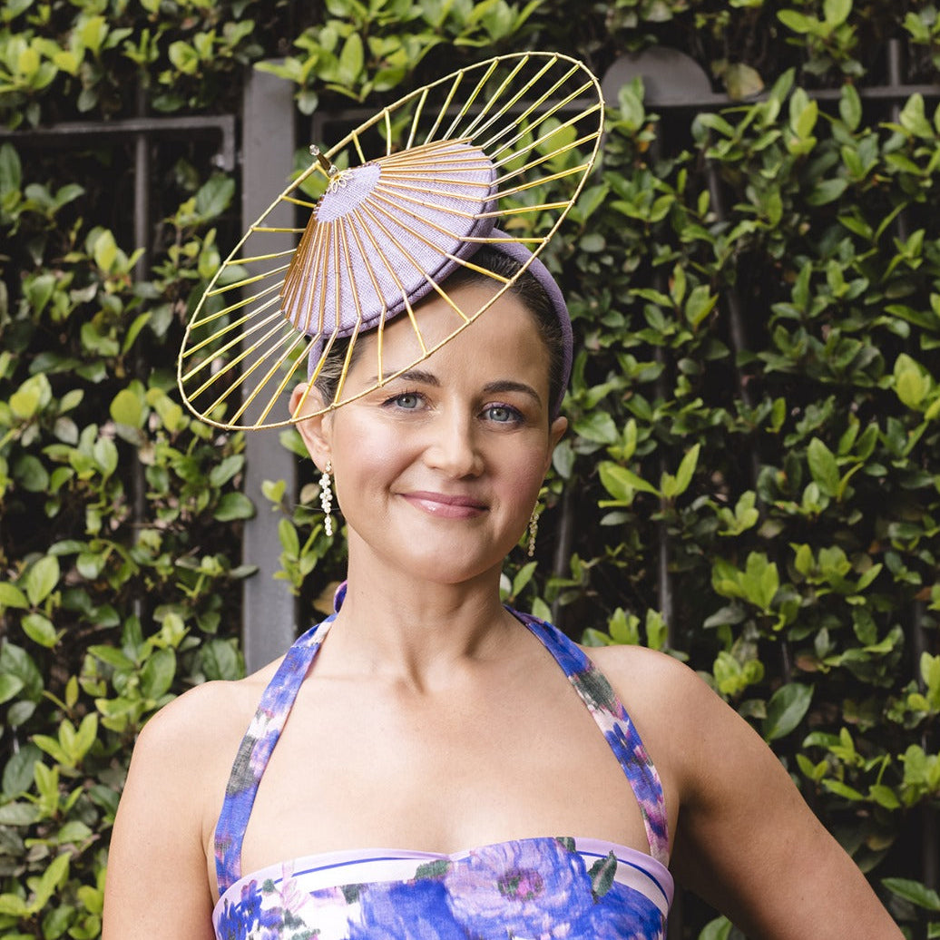 Woman wearing a floral dress and decorative headpiece against a green hedge background