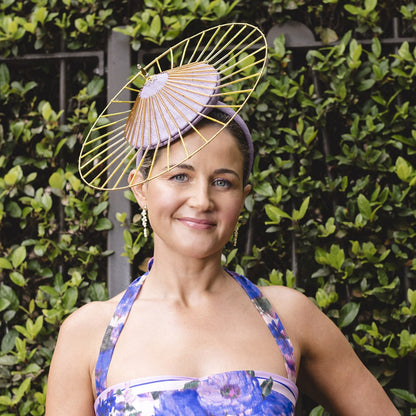 Woman wearing a floral dress and decorative headpiece against a green hedge background