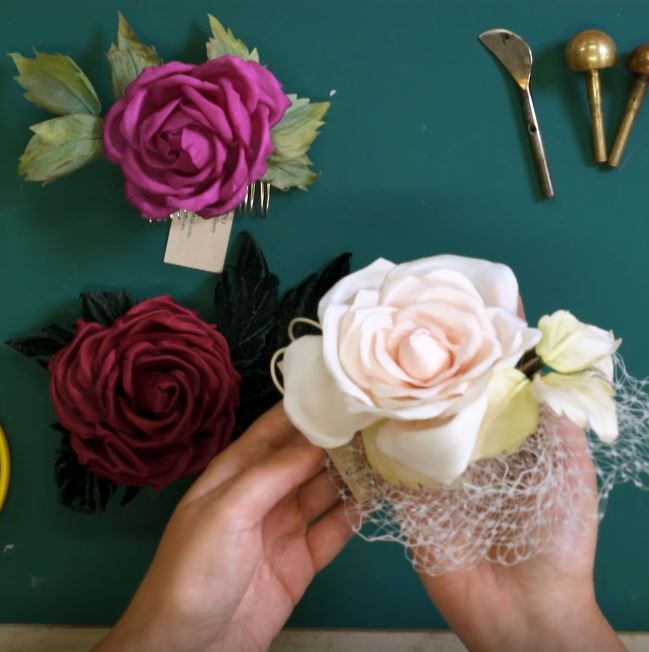 Hand holding a white flower arrangement with other floral decorations on a green surface.
