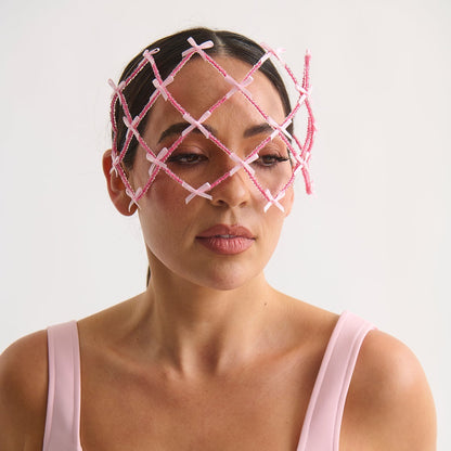 Woman wearing a pink face mask with a lattice design on a white background
