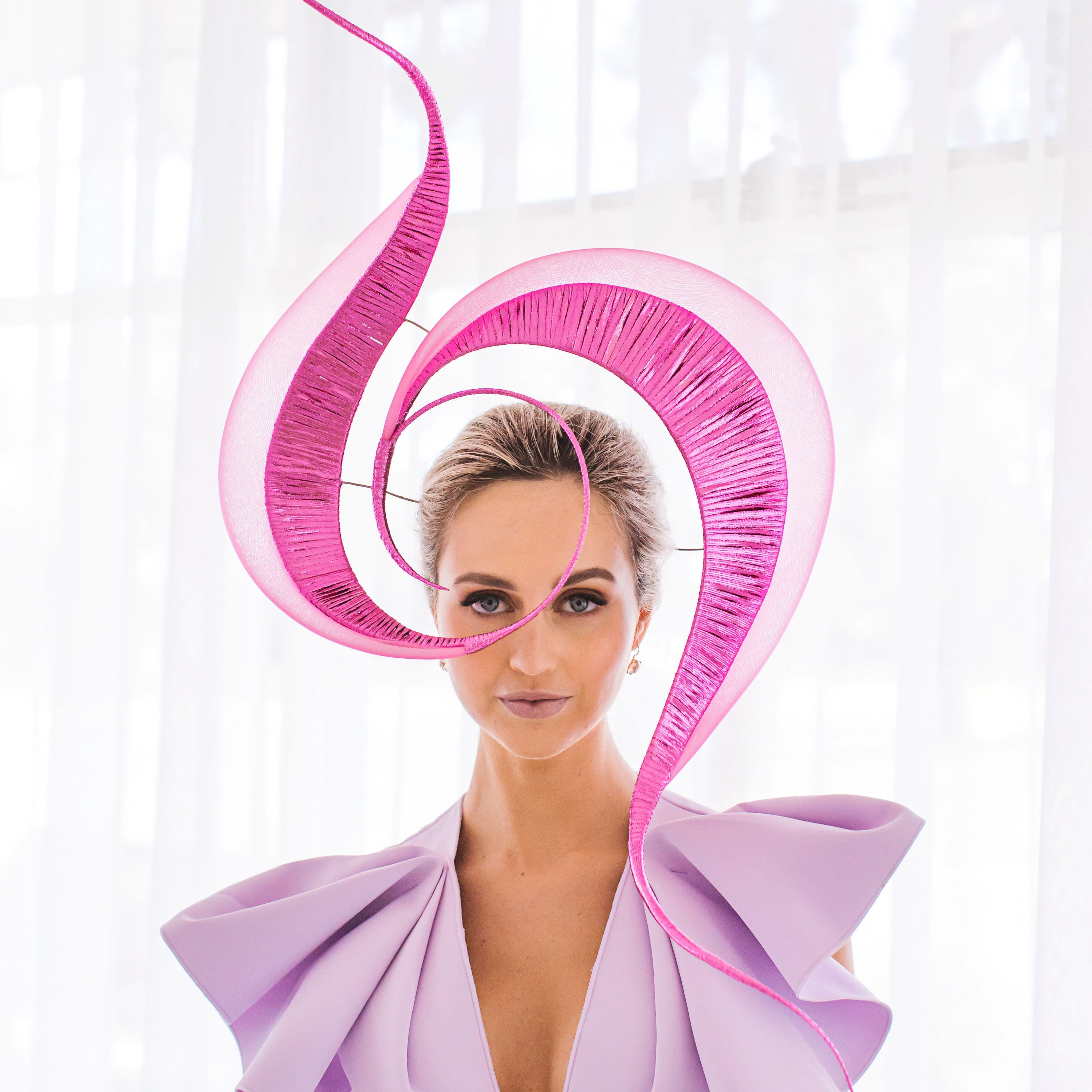 Woman wearing a lavender dress with a large pink decorative headpiece against a white background