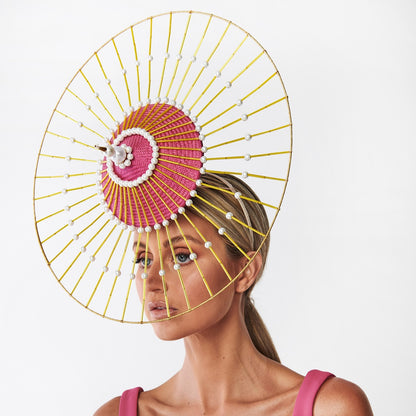 Woman wearing a large decorative headpiece with pink center and gold frame on a white background